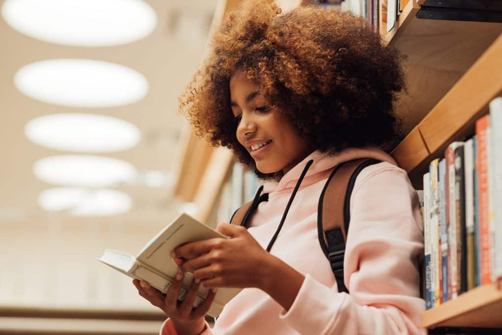 Teen girl reading book in library.