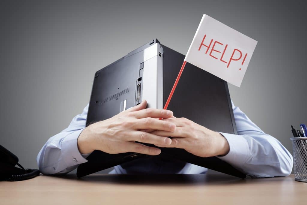 Frustrated man burying his head under a laptop asking for help