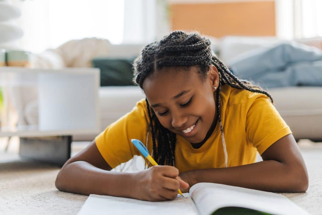 Concentrated happy girl, teenager drawing in sketchbook at home using felt tip pen while lying at the floor. Hobby concept